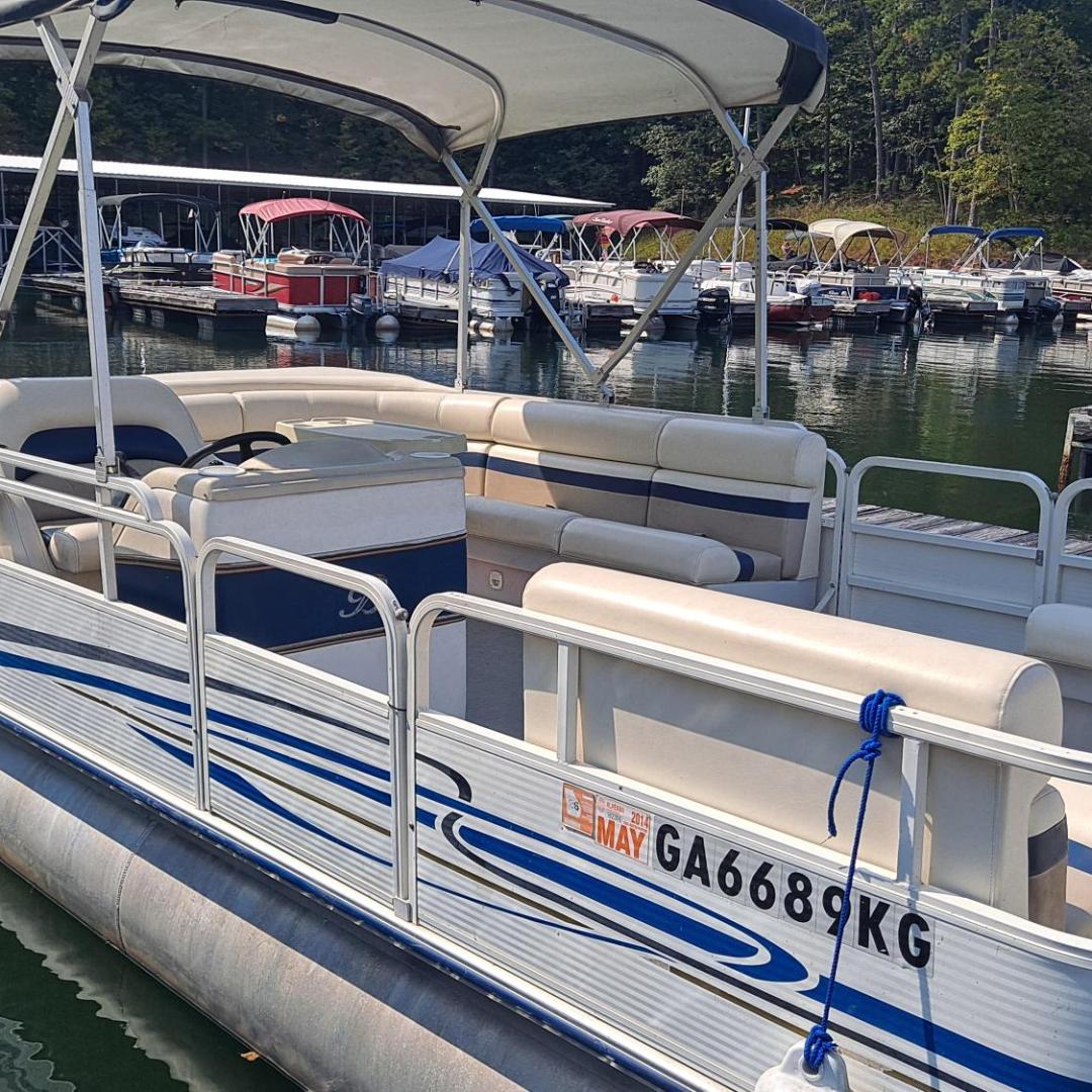 Pontoon boat with canopy moored on a lake, surrounded by other boats at a marina.