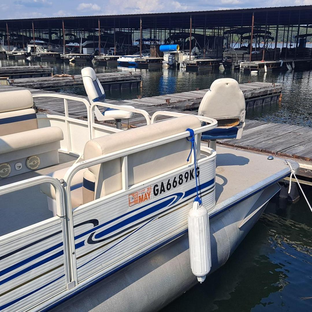 Pontoon boat docked at a marina with covered slips in the background.