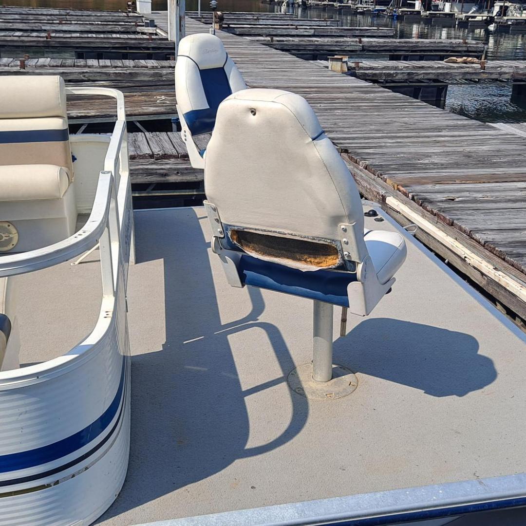 Boat with worn seat docked at marina with wooden piers.