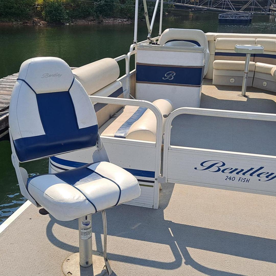 Pontoon boat with white and blue seating, docked by a lake.
