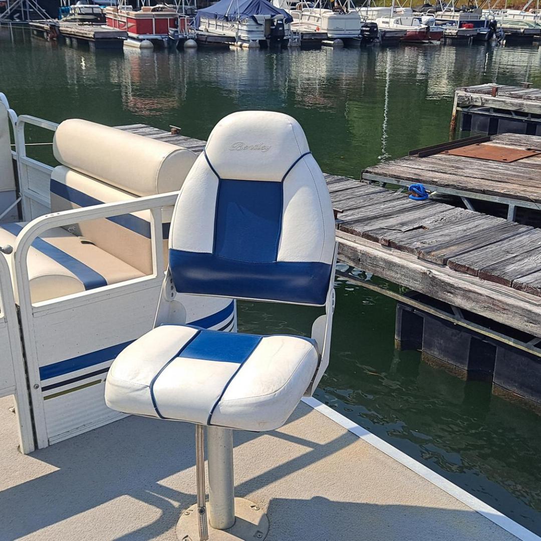 Pontoon boat seat on deck near a marina with floating docks and boats in the background.