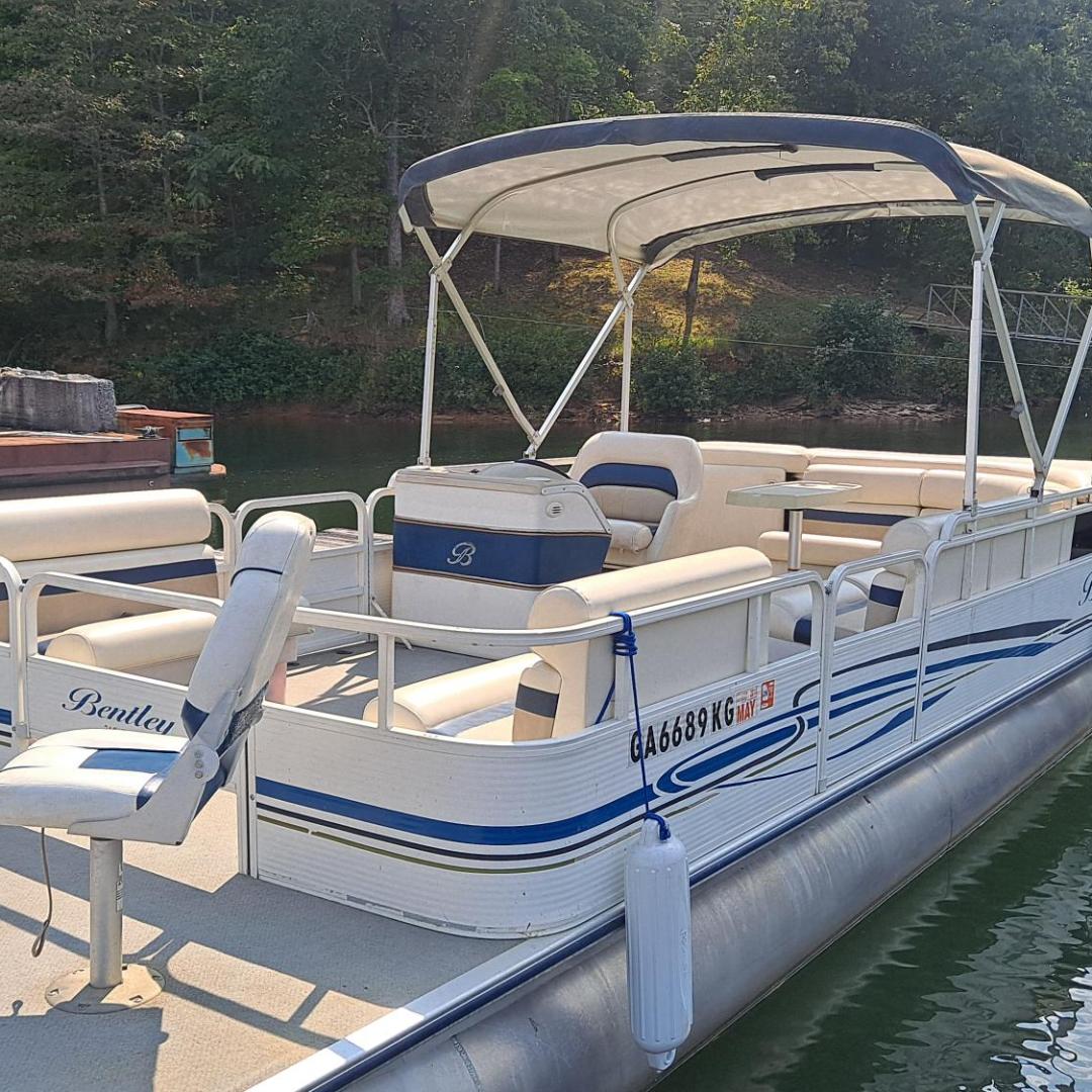 Pontoon boat docked on a lake with trees in the background.