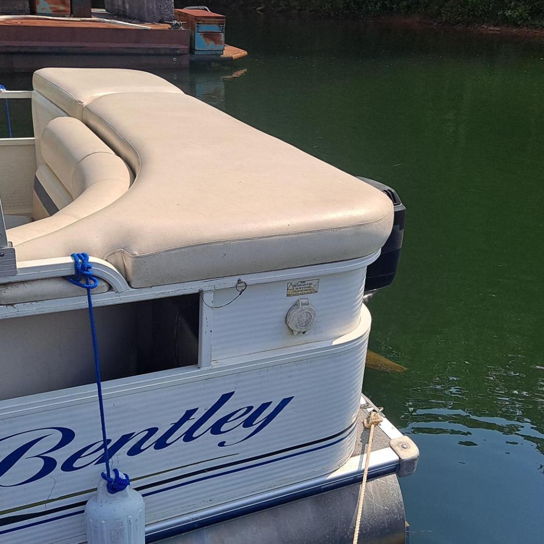 Bentley pontoon boat with beige seats moored in calm green water.