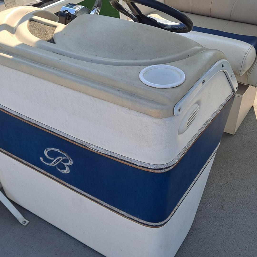 Boat console with steering wheel, two cup holders, and bench seating on a sunny day.