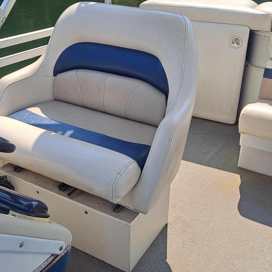 Empty boat seats with steering wheel and water in background.