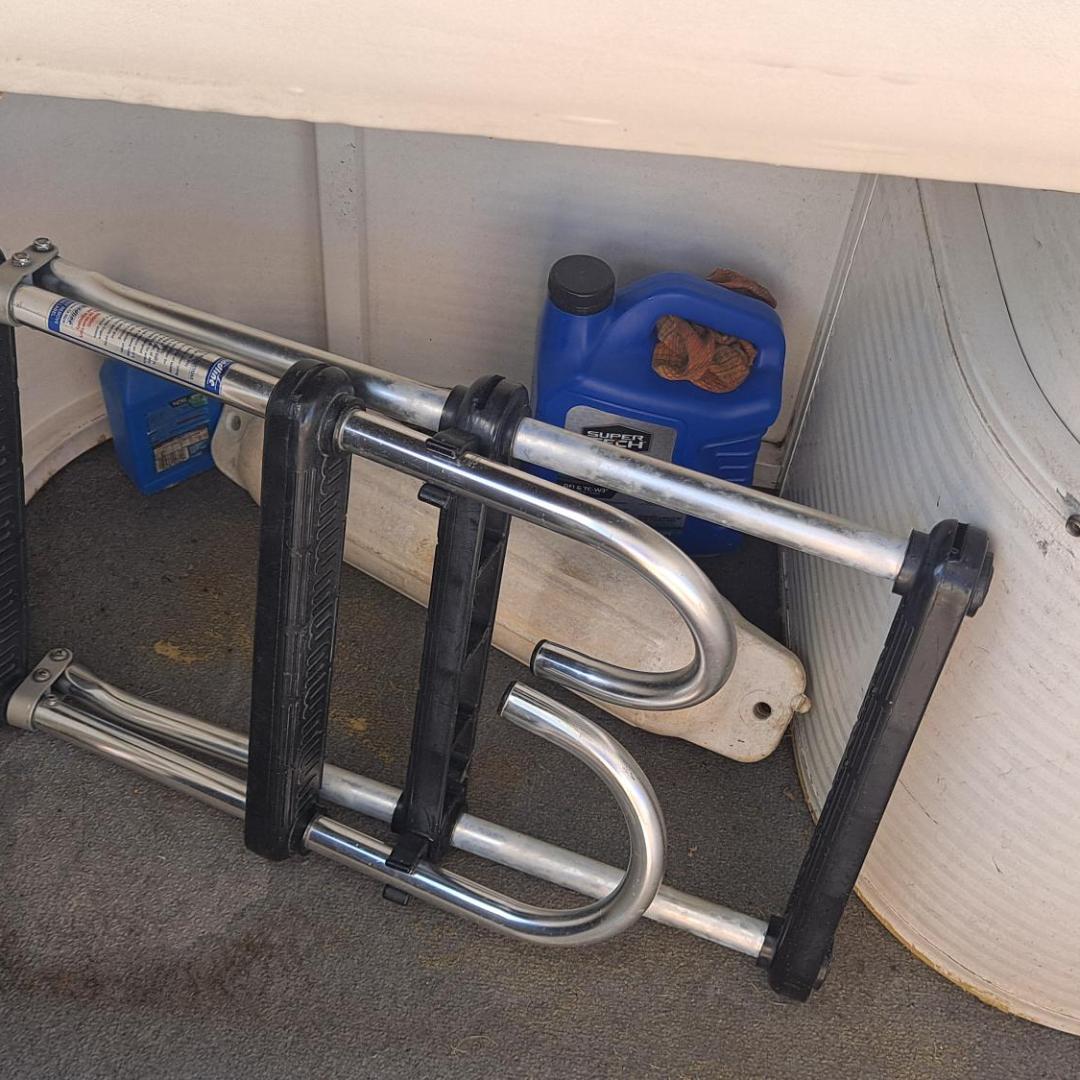Folded metal ladder and blue jugs stored in a small compartment.