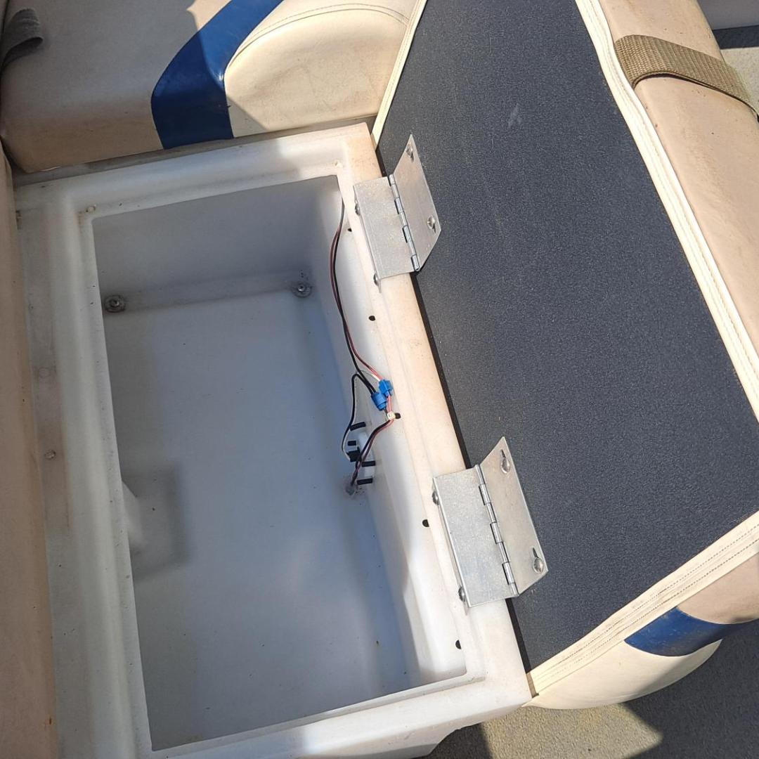 Boat seat storage compartment open, showing empty space and wiring inside.