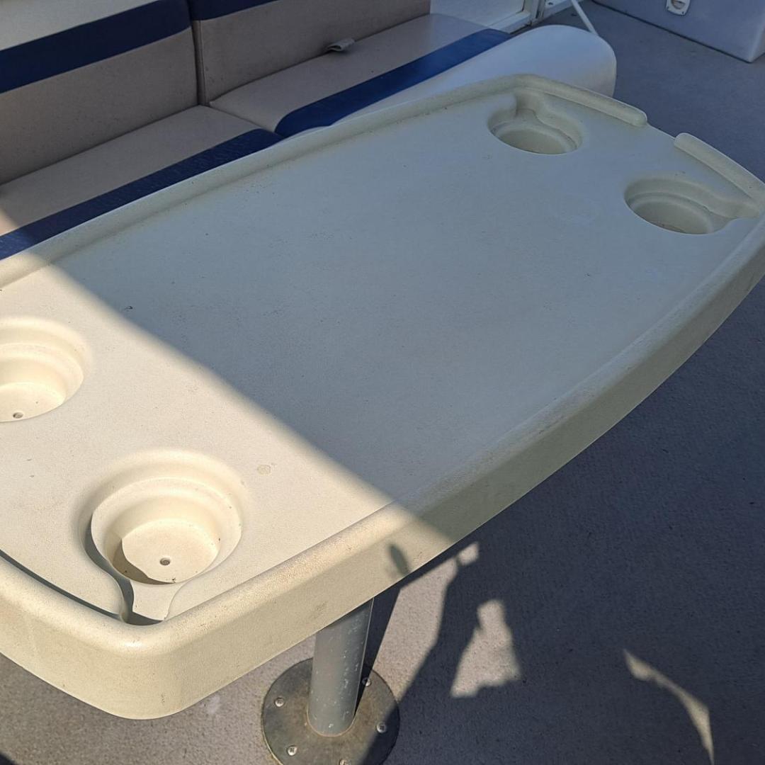 Beige boat table with cup holders on a deck with padded seating.