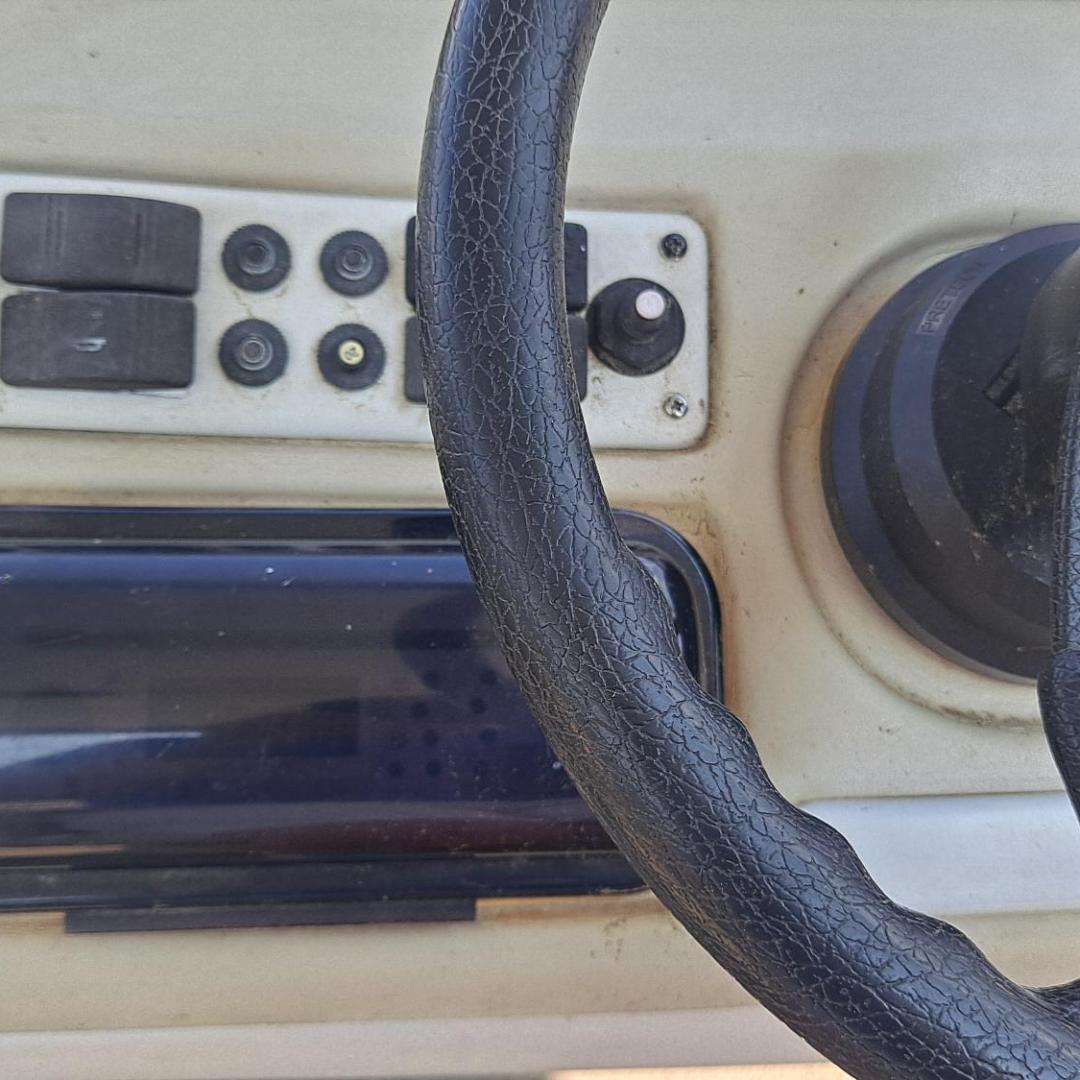 Black steering wheel with a control panel, knobs, and buttons on a beige surface.
