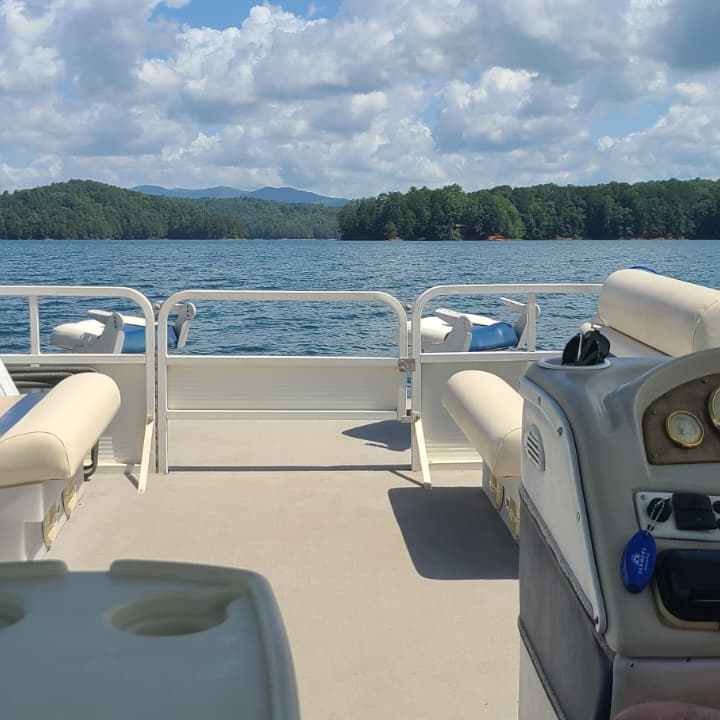 View from a boat's deck with steering wheel, lake and forested hills in background.