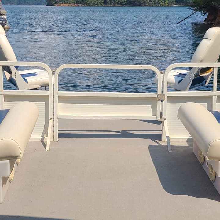 Interior of a pontoon boat with beige seating facing a lake view.