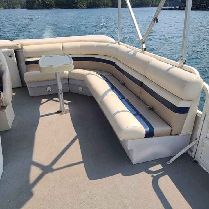 Pontoon boat interior with white seats and canopy on a lake under blue sky.