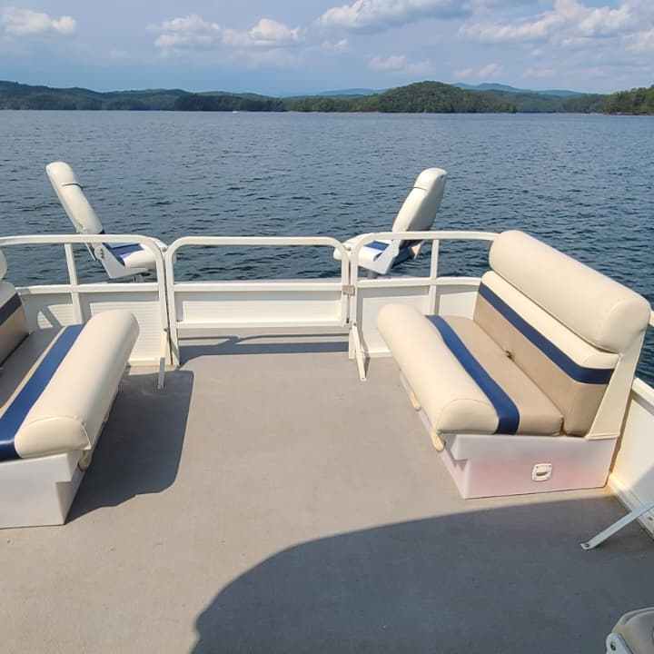 Pontoon boat with empty seats on a calm lake under a partly cloudy sky.