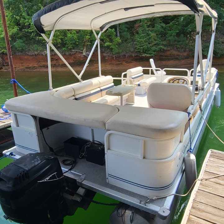 Pontoon boat docked under a covered structure on a green water lake.