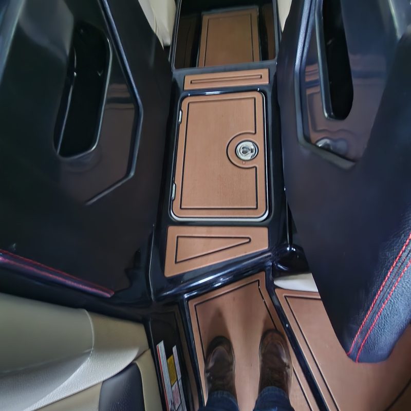 Interior of a vehicle showing console, cup holder, and person's legs with brown shoes.