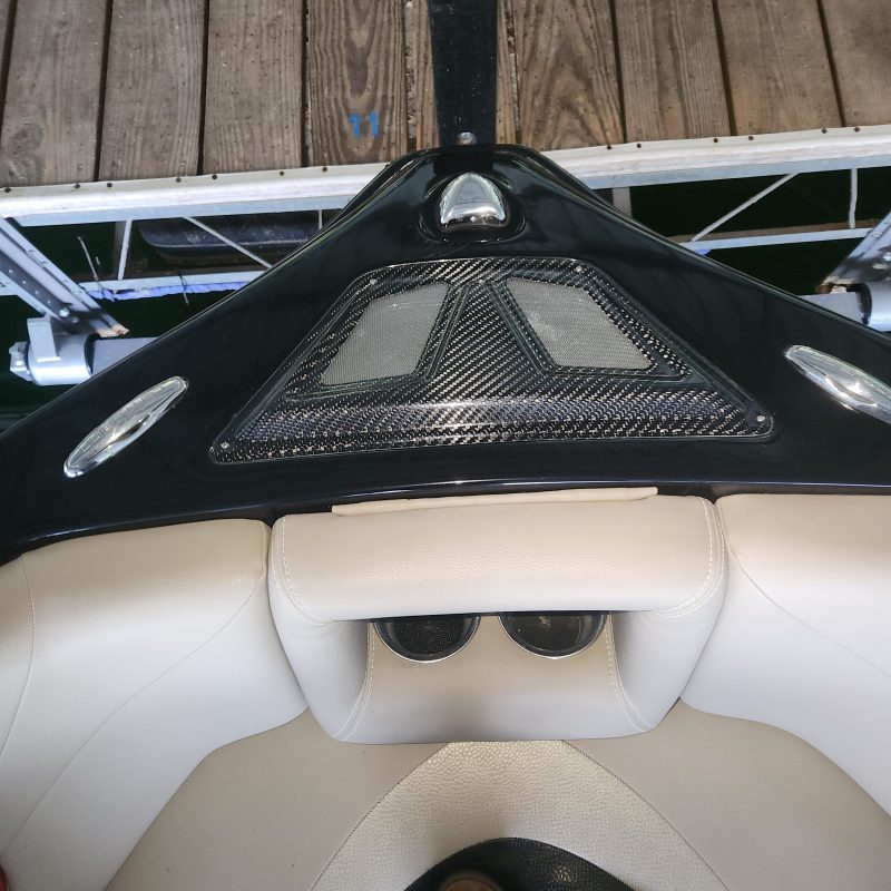 Front view of a boat with white seats and black dashboard, docked at a wooden pier.