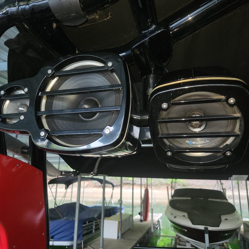 Two black speakers mounted on a metal bar under a boat canopy.