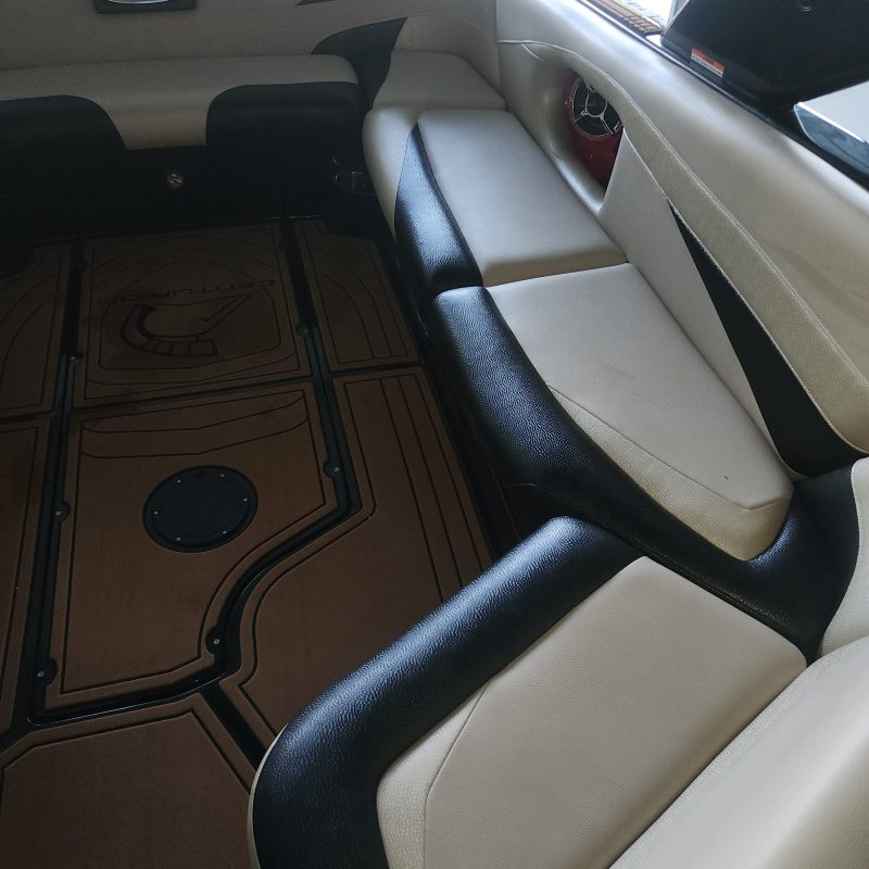 Interior of a boat with white and black seating and brown flooring.
