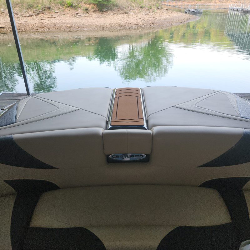 Boat interior with tan and black seats overlooking water and trees.
