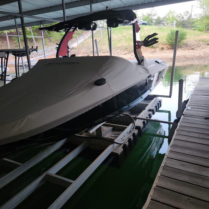 Boat on a lift in a covered dock with nearby trees visible.