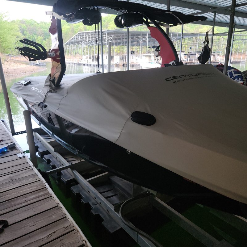 Covered boat with wakeboards stored in a metal-roofed dock area.