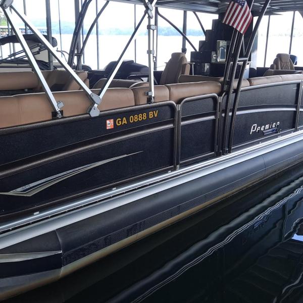 Black pontoon boat with seating and canopy on a calm lake.