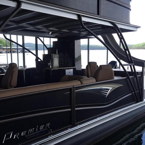 Pontoon boat with flag docked by a calm lake.