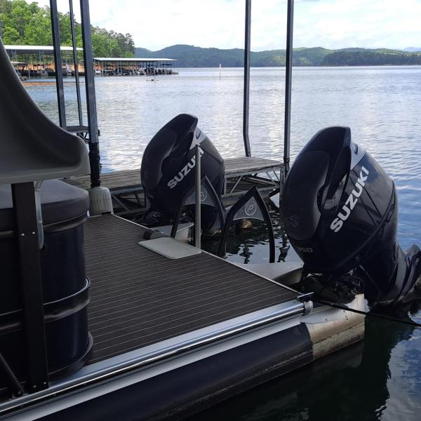 Boat docked by a lake with two Suzuki outboard motors.