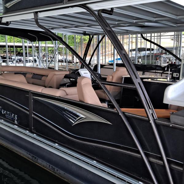 Black pontoon boat with slide docked in marina.