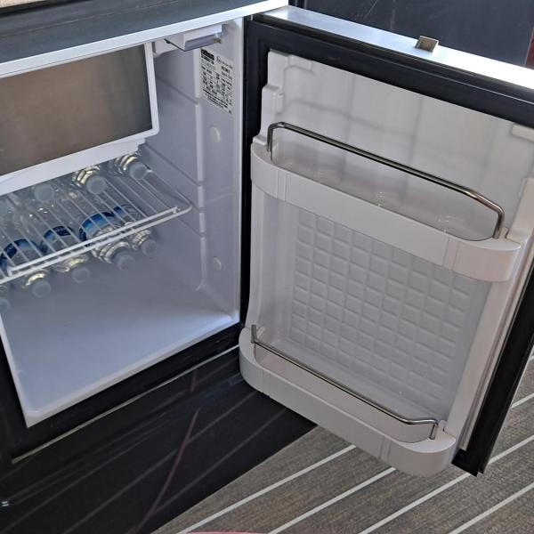 Open mini-fridge with drinks inside on a wooden floor.