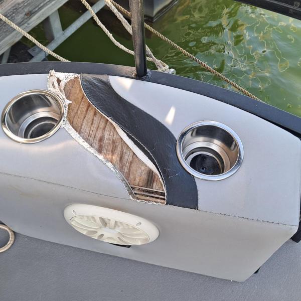 Damaged boat panel with cup holders and speaker near water.