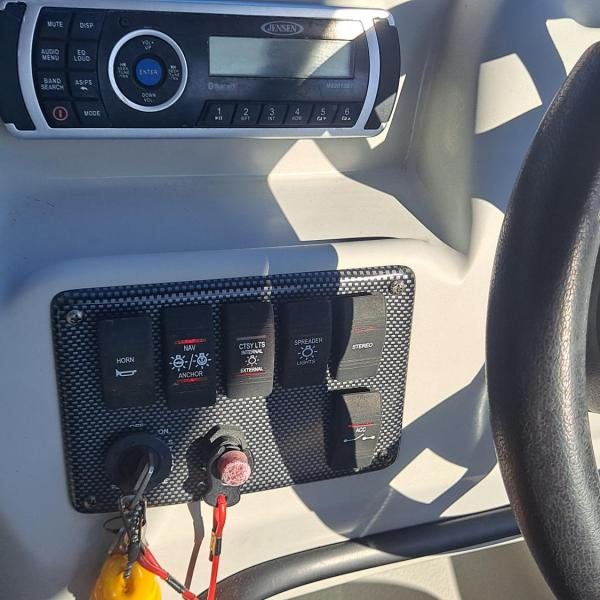 Boat dashboard with steering wheel, radio, and control panel with switches.