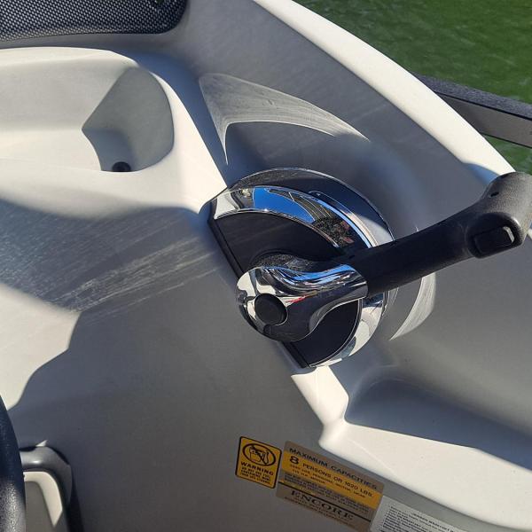 Close-up of a boat throttle lever and steering wheel by water.