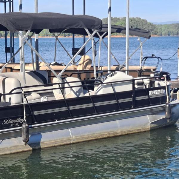 Black pontoon boat docked on a lake with a canopy.