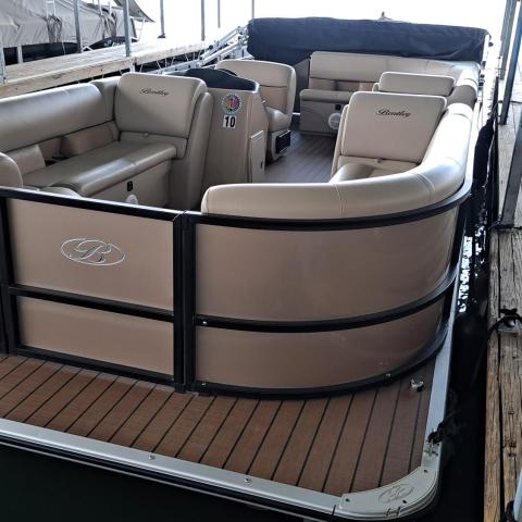 Beige pontoon boat docked on a wooden pier with cushioned seating and a covered console.
