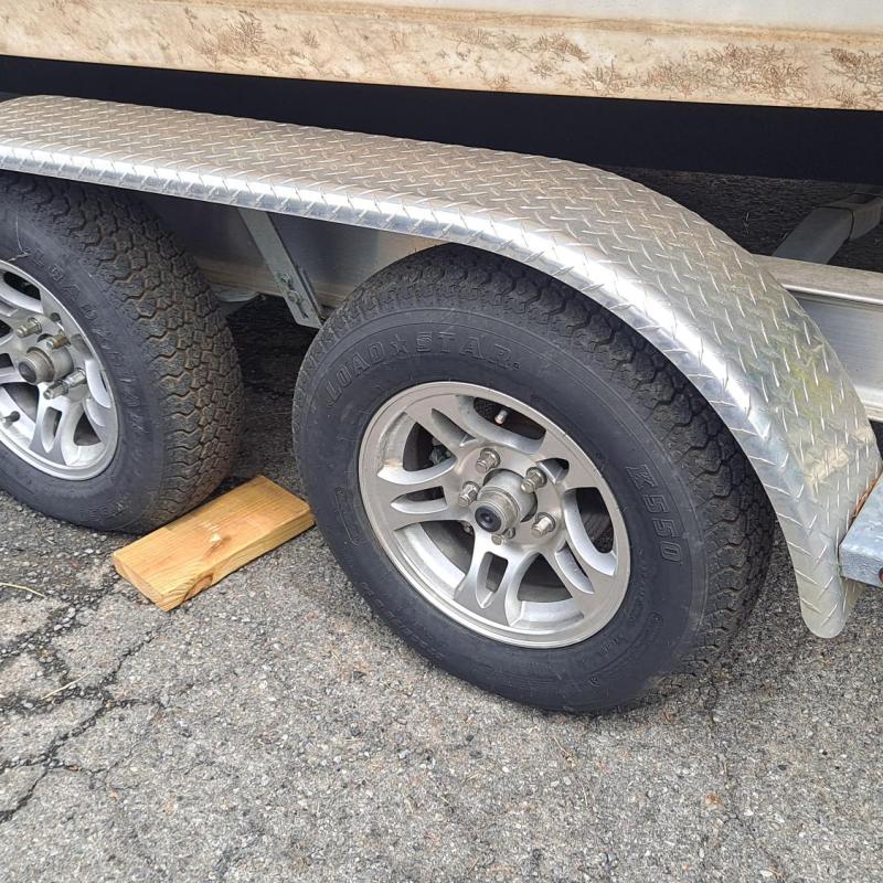 Tandem trailer wheels with a wooden chock on rough pavement.